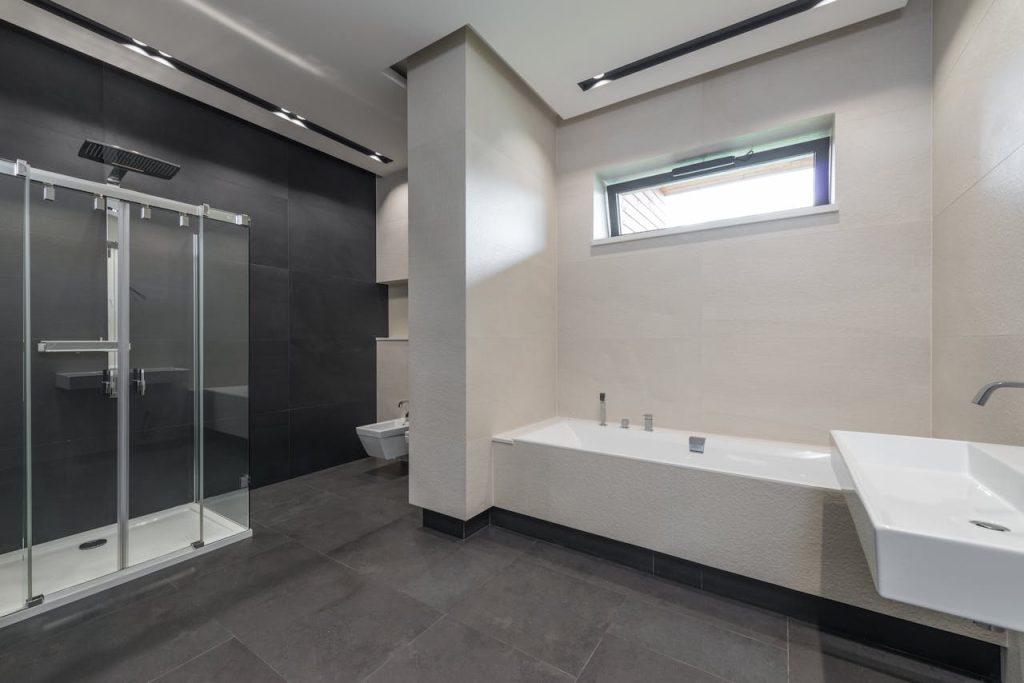 Interior design of contemporary spacious bathroom with shower cabin and bathtub in white and gray tones in modern house